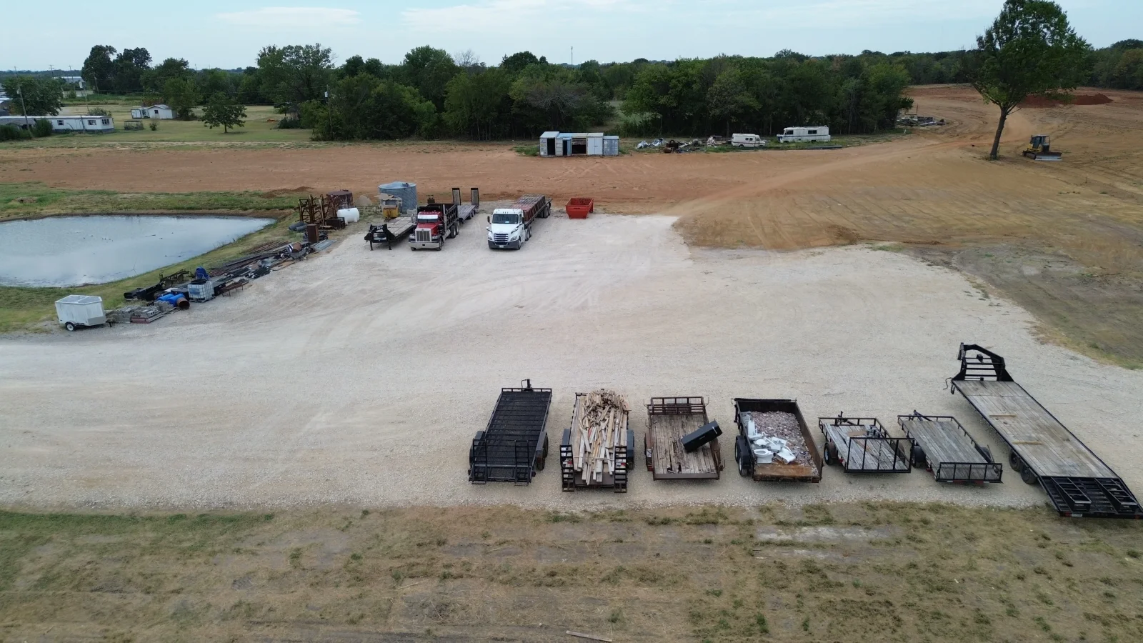 Aerial view of gravel lot with utility trailers, flatbeds, and commercial vehicles parked in organized rows