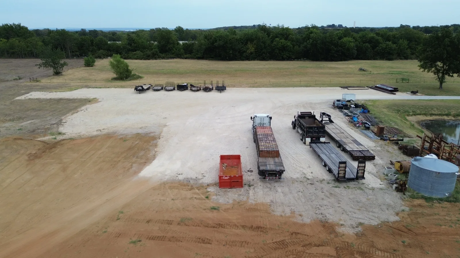 Concrete parking lot with agricultural trailers, trucks, and equipment on rural property