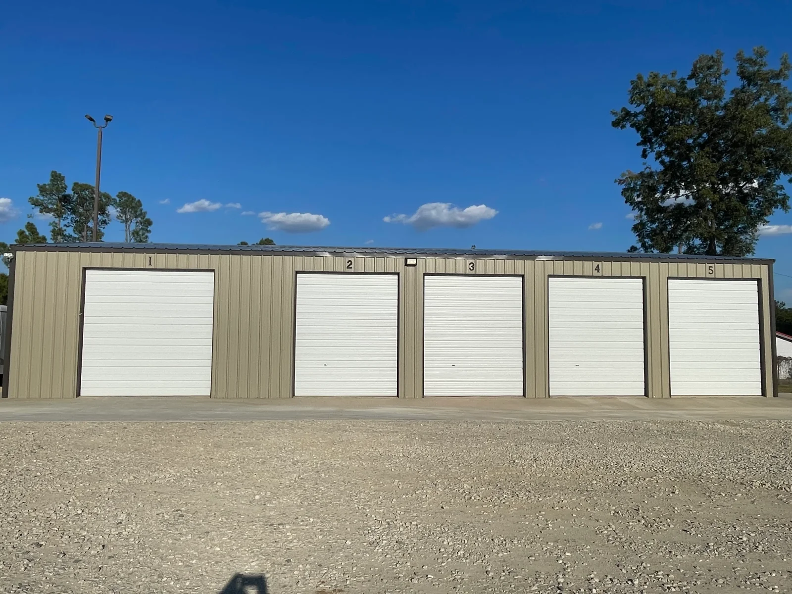 Five-bay metal storage building with white roll-up doors and tan corrugated steel siding